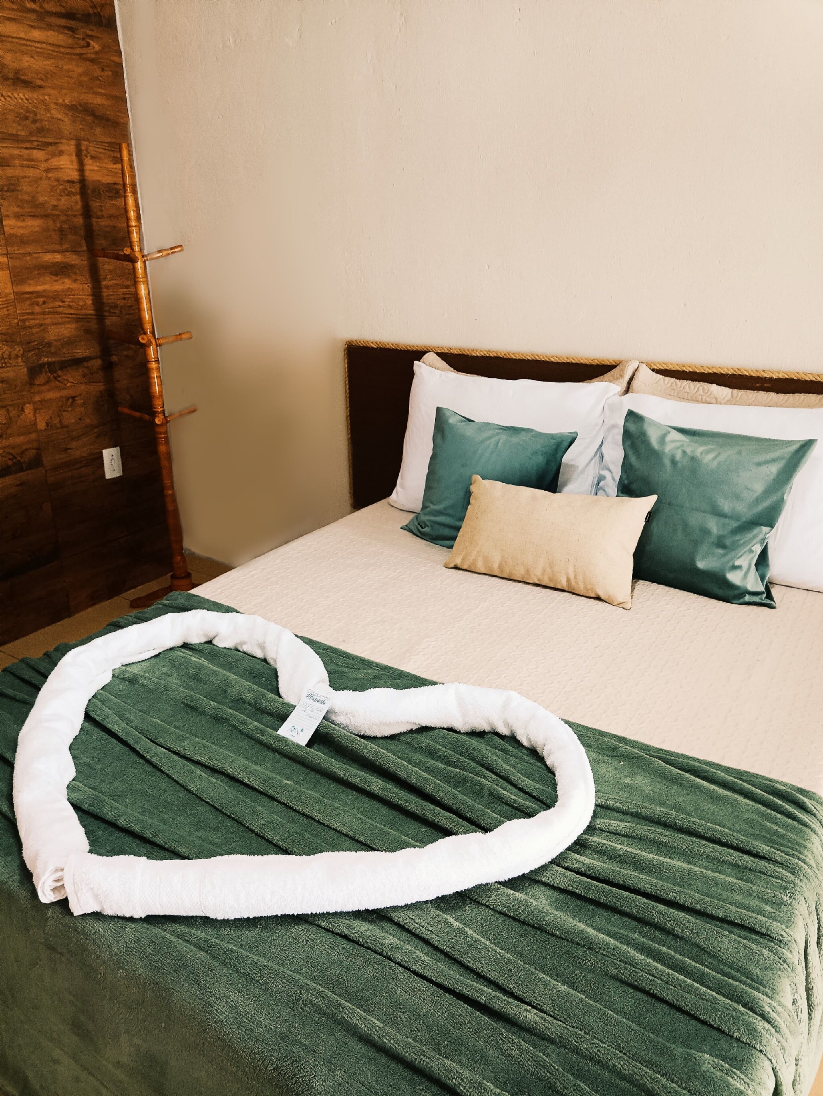 A neatly made bed with a green blanket and white pillow, a wooden headboard, and a wooden floor.
