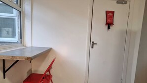 A room with a white door, a red fire alarm, a window, and a red chair. - Easy Rooms - London Luton Airport (Luton)