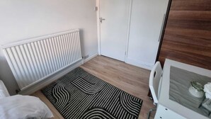 A room with a white door, a radiator, a patterned rug, and a white cabinet with a glass door. - Easy Rooms - London Luton Airport (Luton)