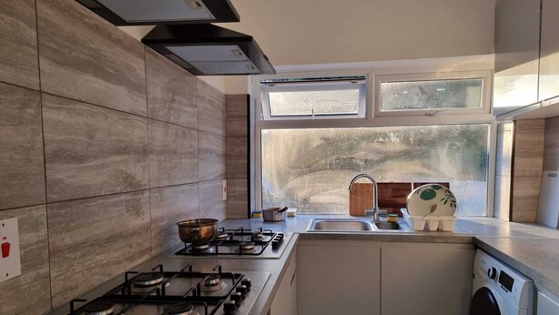A modern kitchen with a gas stove, a built-in oven, a washing machine, and a window with a view of the outdoors. - Easy Rooms - London Luton Airport (Luton)