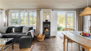 A cozy living room with a fireplace, a sofa, a dining table, and large windows.