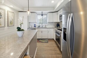 A modern kitchen with white cabinetry, stainless steel appliances, and a marble countertop.