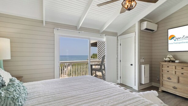 A bedroom with a bed, a dresser, a ceiling fan, and a view of the ocean.