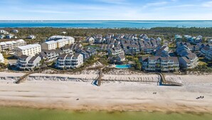 An aerial view of a coastal residential area with beachfront properties, a boardwalk, and a clear view of the ocean.