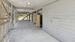 A covered outdoor area with a concrete floor, wooden fencing, and a staircase leading to an upper level.