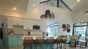 A modern kitchen with white cabinets, a central island with bar stools, and pendant lighting. - Casa Coral Azul (Cahuita)
