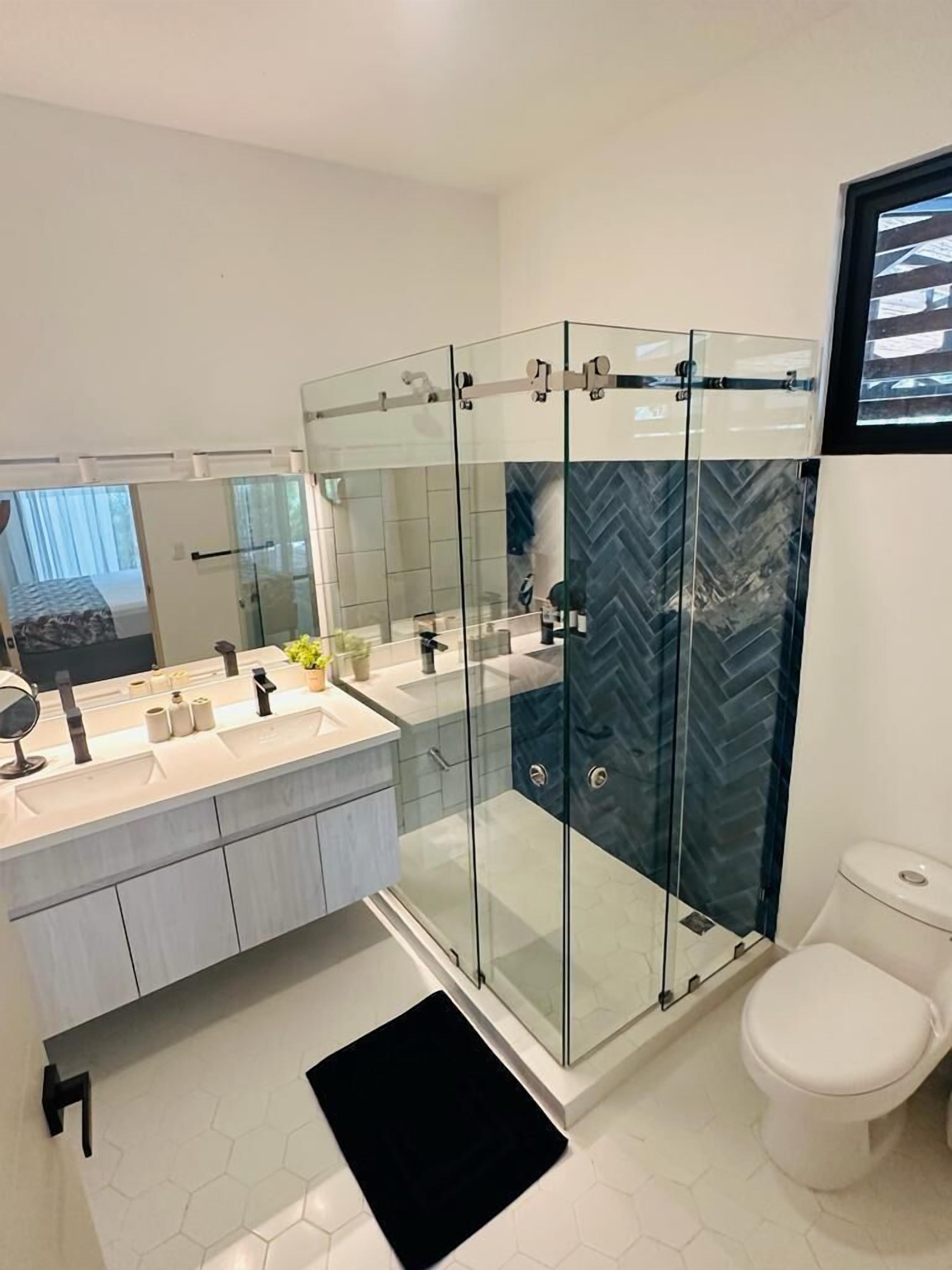 Un baño moderno con ducha envuelta en vidrio, inodoro blanco y tocador con un espejo grande.