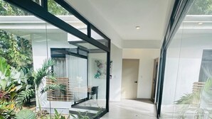 A modern interior with a glass partition, a tiled floor, and a small garden area with plants. - Casa Coral Azul (Cahuita)