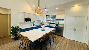 A modern kitchen with a large island, white cabinetry, and a stainless steel refrigerator. - Casa Coral Azul (Cahuita)