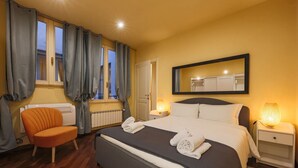 Et hotelværelse med seng, stol, natbord, lampe og et vindue med gardiner.