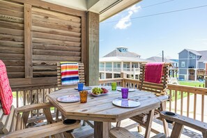 A wooden deck with a table set for dining, featuring plates, glasses, and a bowl of fruit. - Steps to Beach, Hot Tub, Gulf & Beach Views, Tiki Bar, Grill, Dogs, Games (Bolivar Peninsula)