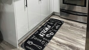 A modern kitchen with white cabinets, black backsplash, stainless steel appliances, and a black and white kitchen mat.