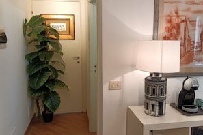 A hallway with a potted plant, a framed picture on the wall, a lamp, and a coffee maker on a table. - Leonardo - Sweet Dreams in Florence (Firenze)