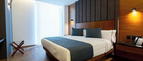 A modern bedroom with a large bed, wooden headboard, and a bedside table with a phone.
