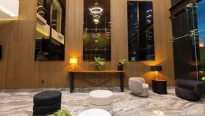Un interior moderno con un panel de madera, una puerta de cristal y una zona de estar con otomanas y una mesa redonda.