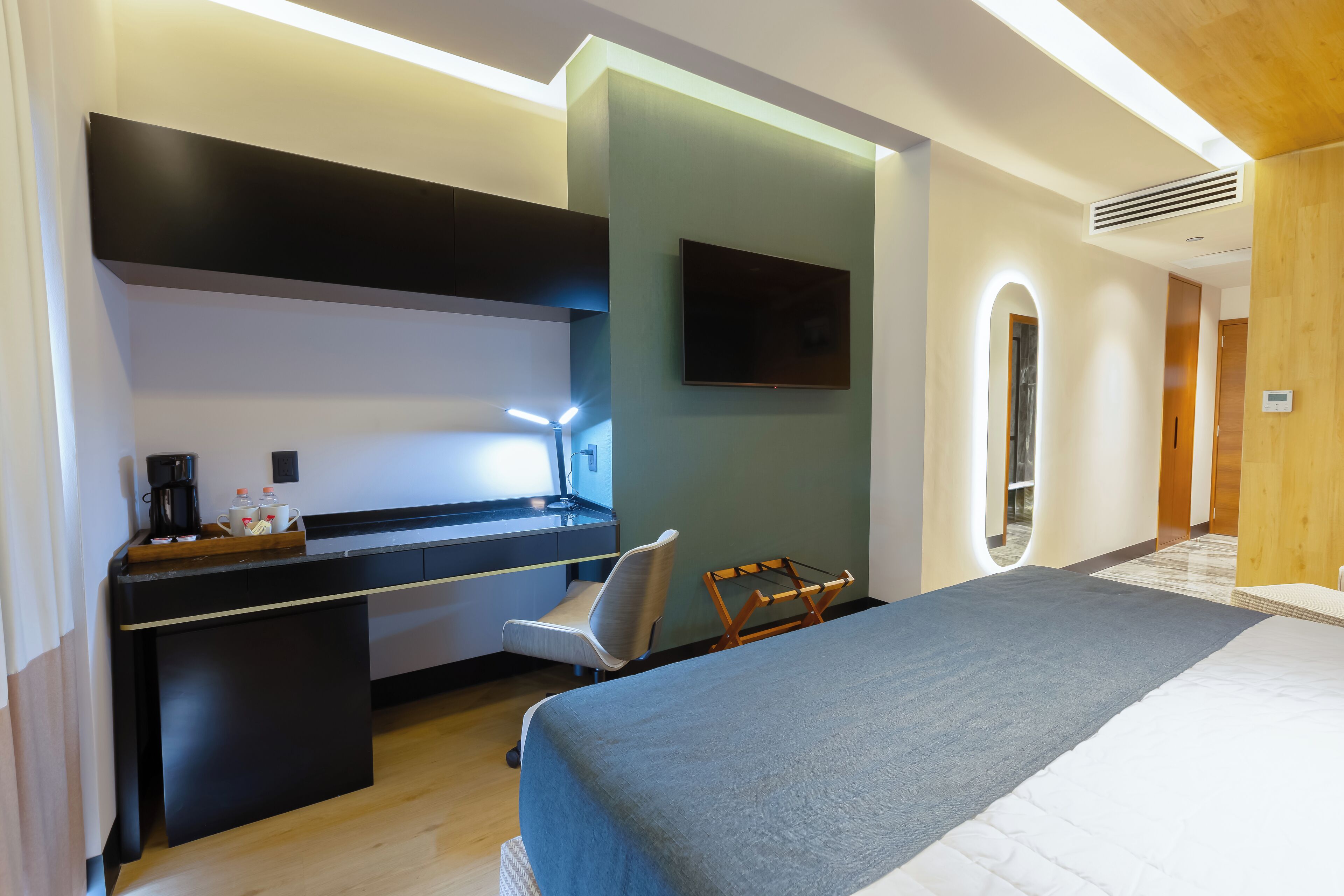 Una habitación de hotel moderna con una cama, un escritorio, una silla y un televisor montado en la pared.