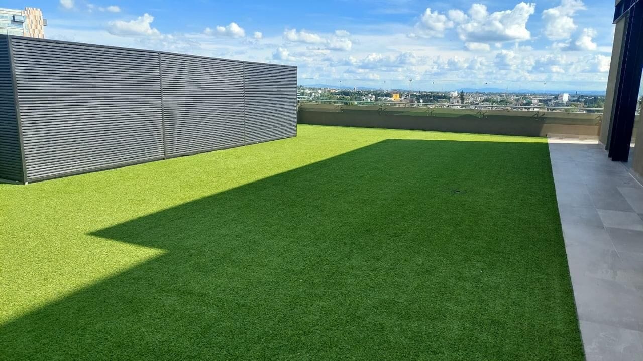 A rooftop terrace with artificial grass, a metal fence, and a cityscape view.