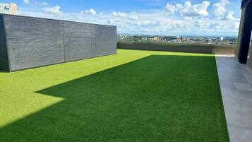 Una terraza en la azotea con césped artificial, una barandilla de metal y vistas a la ciudad.