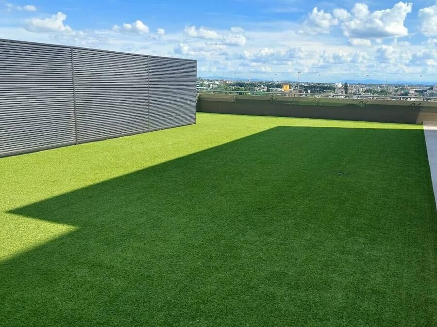 Una terraza en la azotea con césped artificial, una barandilla de metal y vistas a la ciudad.