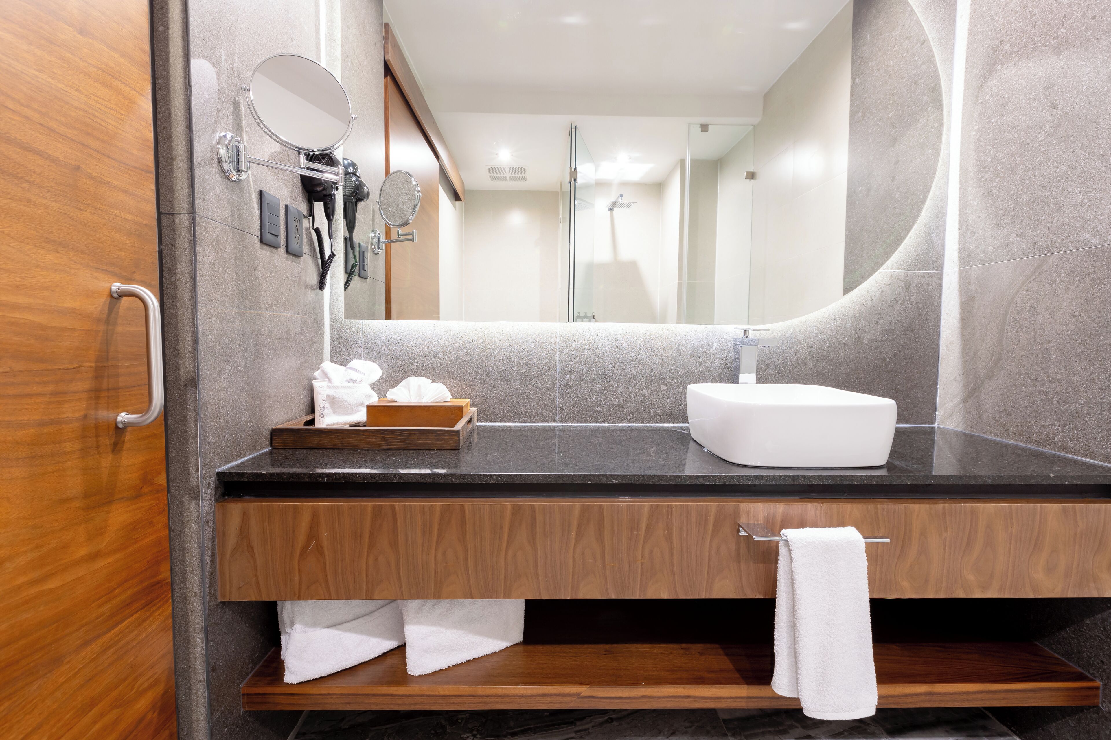 A modern bathroom with a wooden vanity, a white sink, and a large mirror.