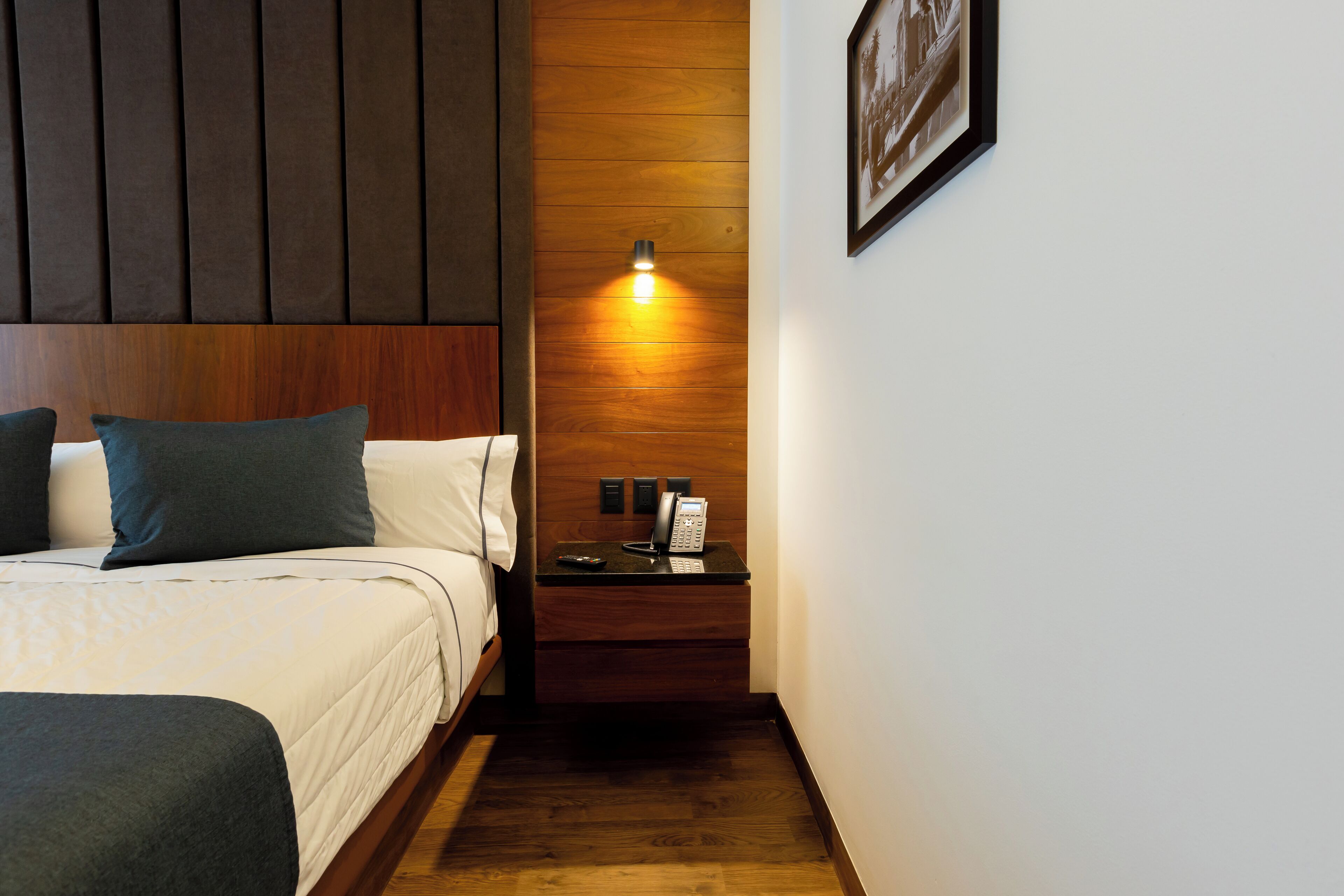 A hotel room with a bed, bedside table, and a wall-mounted light fixture.