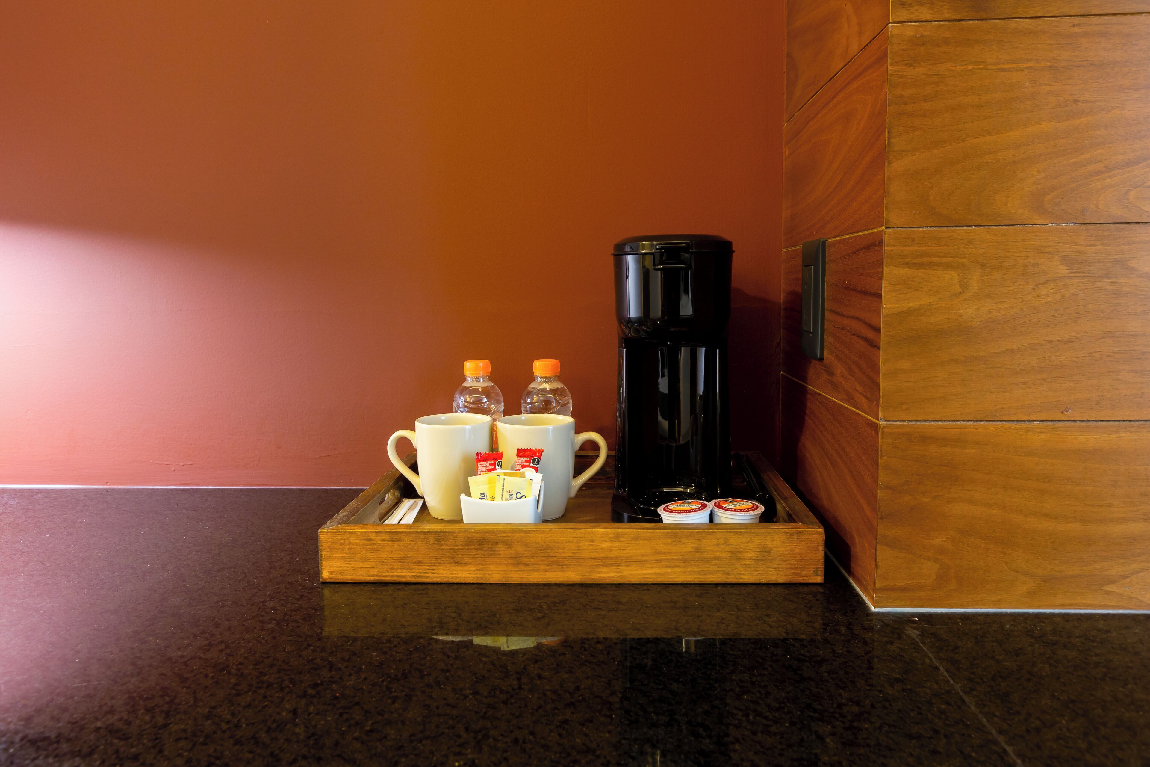A tray with a coffee maker, two cups, and two condiment packets on a countertop.
