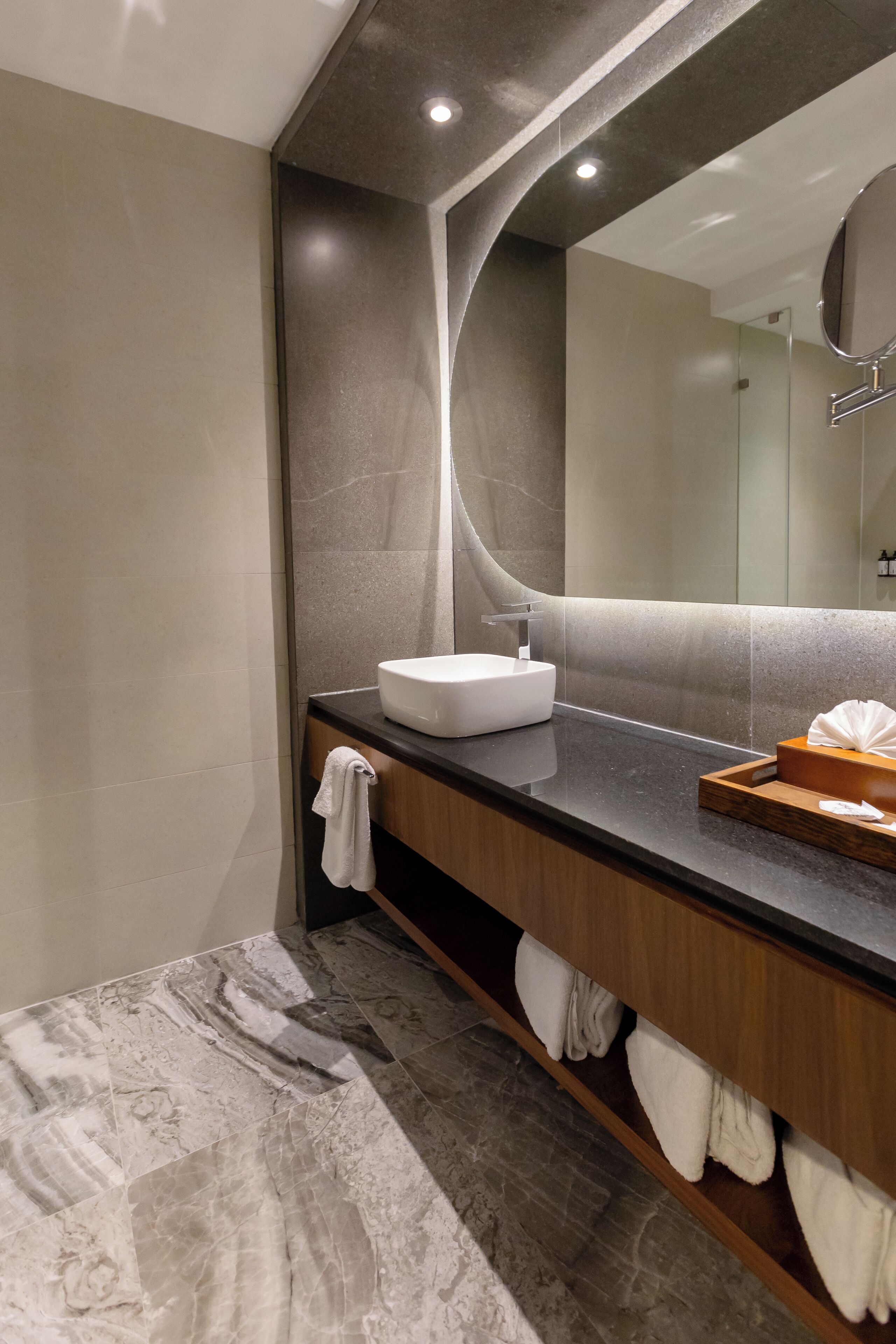 A modern bathroom with a marble floor, a white sink, and a wooden vanity.