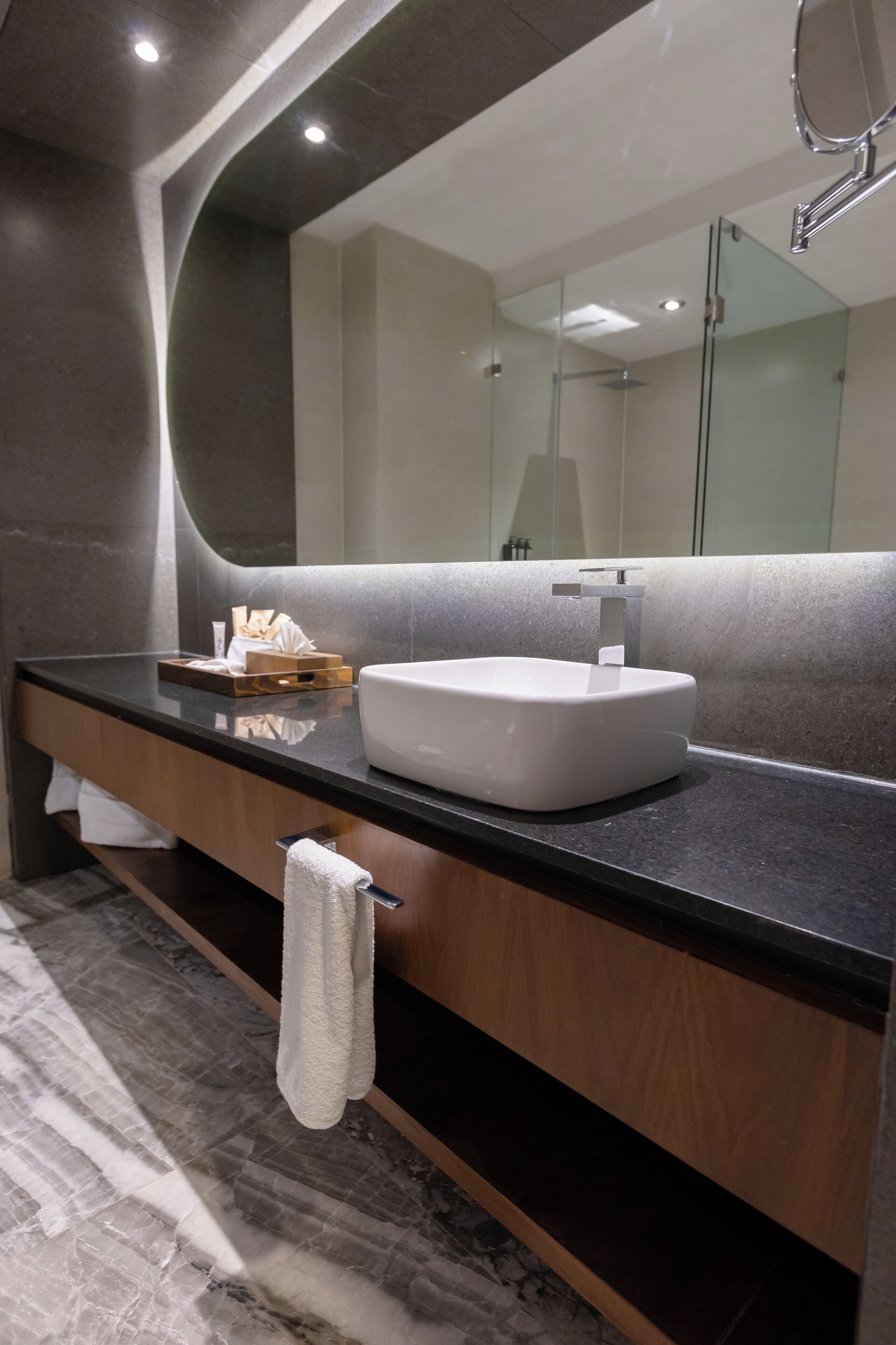 A modern bathroom with a marble floor, a black countertop, a white sink, and a large mirror.