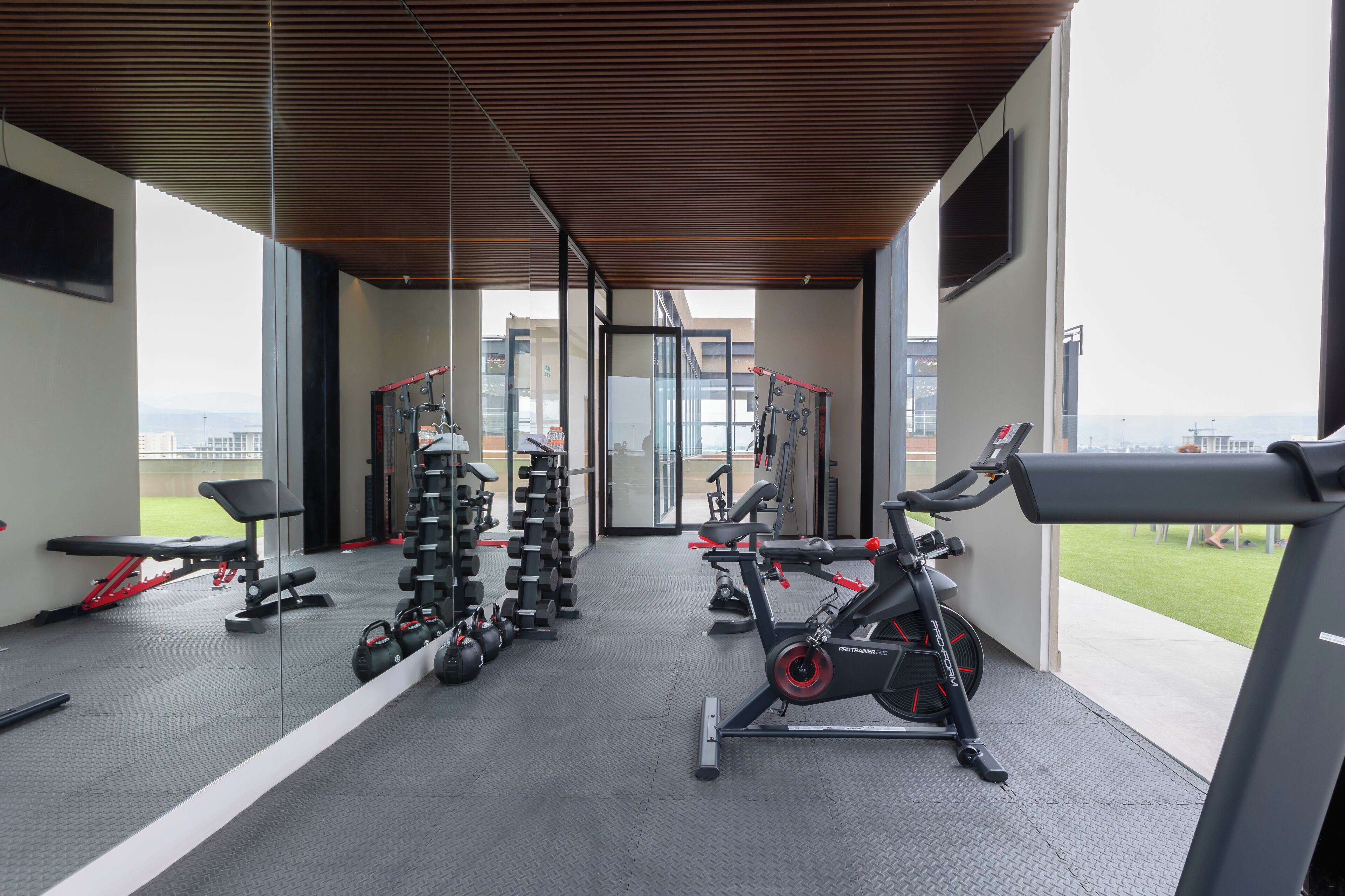 Un gimnasio moderno con diversos equipos de ejercicio, ventanas amplias y vistas a la ciudad.