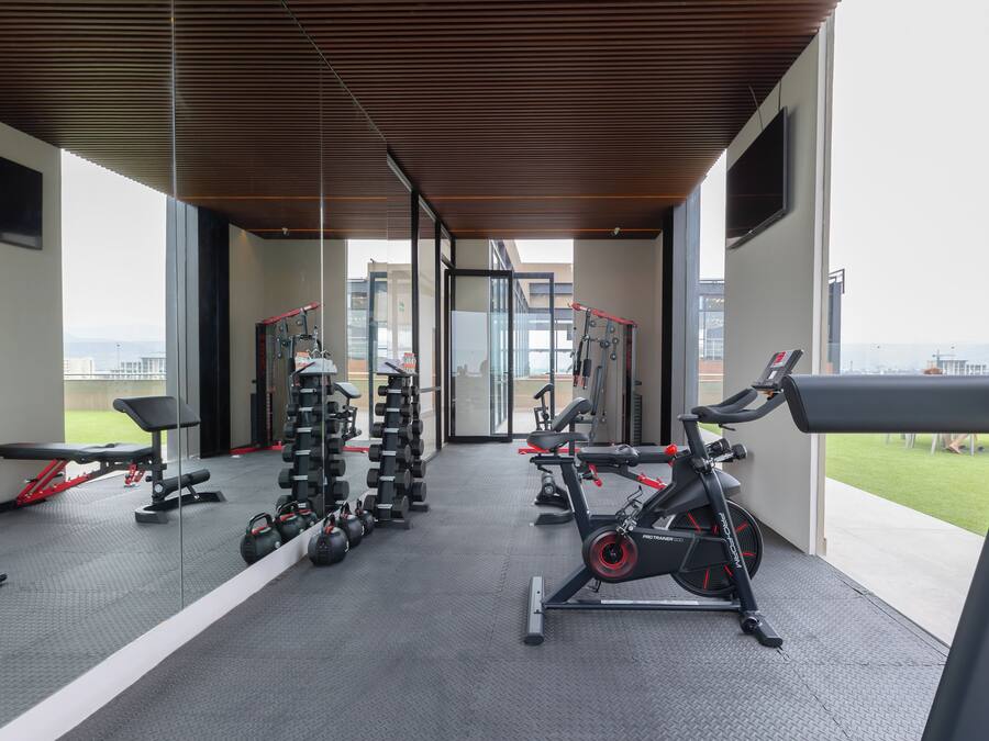 Un gimnasio moderno con diversos equipos de ejercicio, ventanas amplias y vistas a la ciudad.