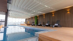 Zona de piscina con sillones reclinables, terraza de madera y un área de estar techada con vista al mar.