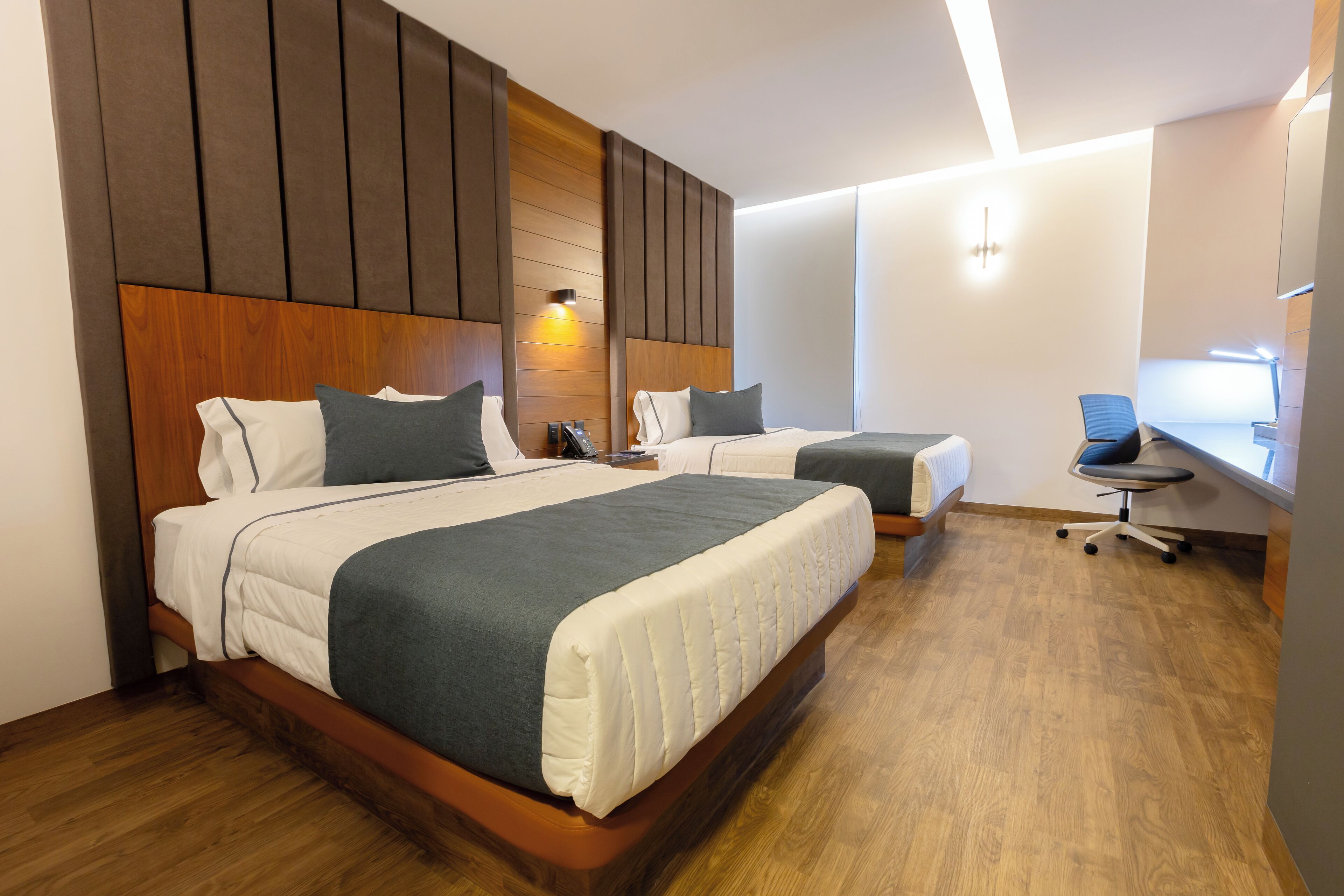 Habitación de hotel con dos camas, cabeceros de madera, un escritorio y una silla.