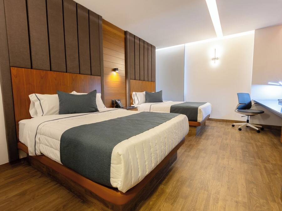 Habitación de hotel con dos camas, cabeceros de madera, un escritorio y una silla.