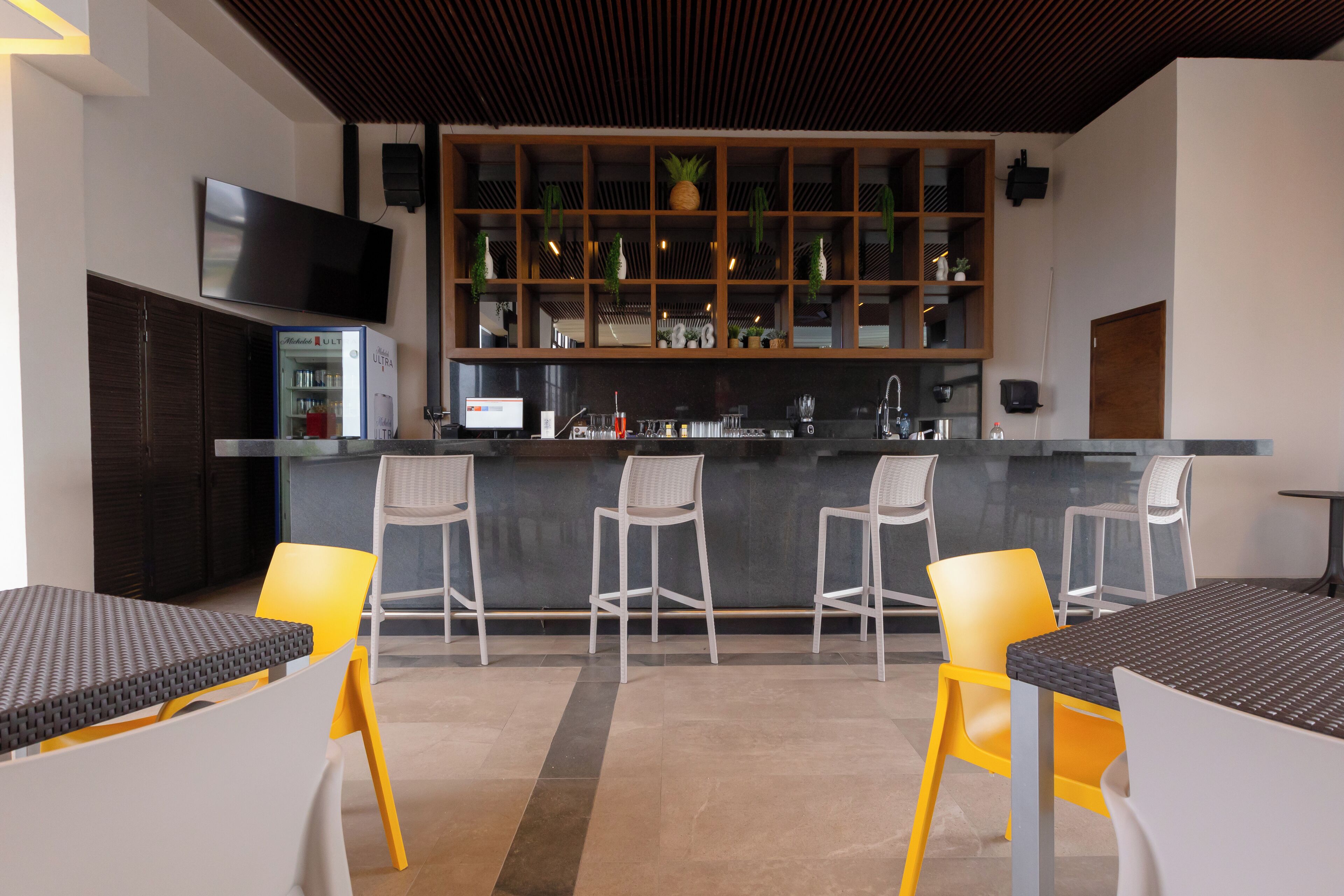 Una cocina moderna con barra, que incluye un televisor de pantalla plana, un refrigerador y taburetes de bar.