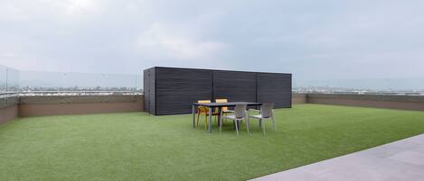 A rooftop terrace with artificial grass, a table with chairs, and a modern fence.