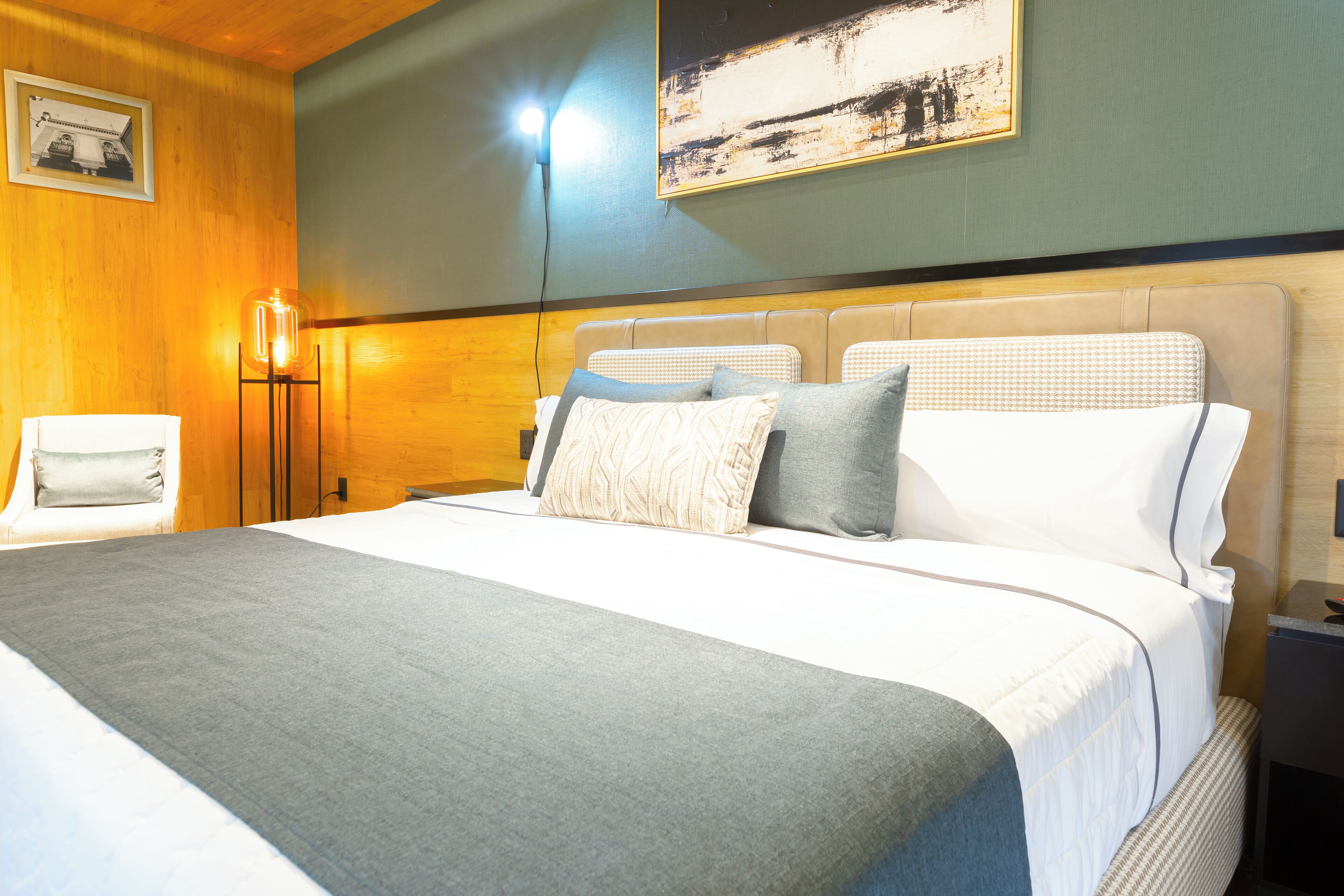 A hotel room with a large bed, a bedside table, a lamp, and a painting on the wall.