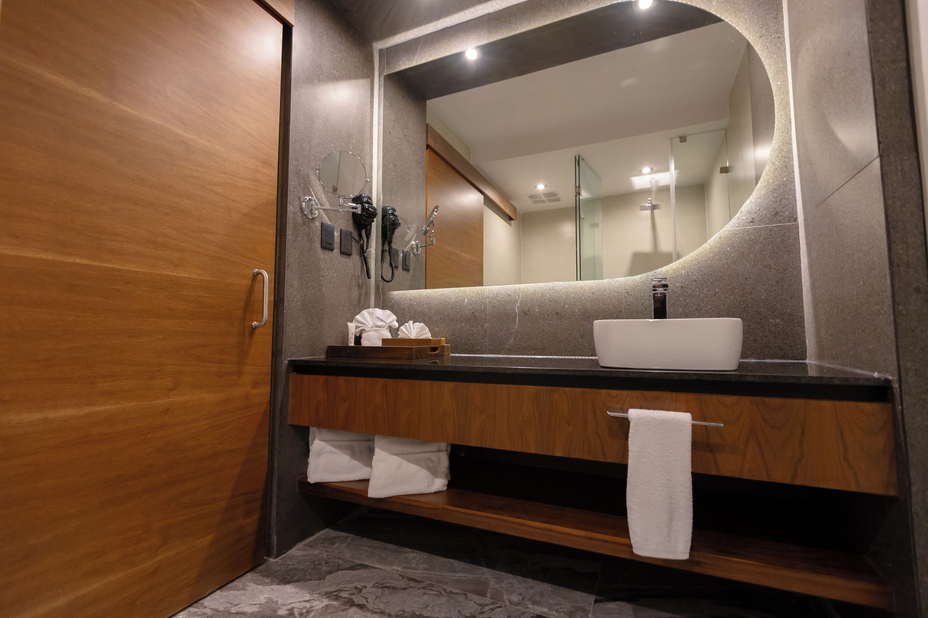 A modern bathroom with a wooden vanity, a large mirror, and a built-in shower.