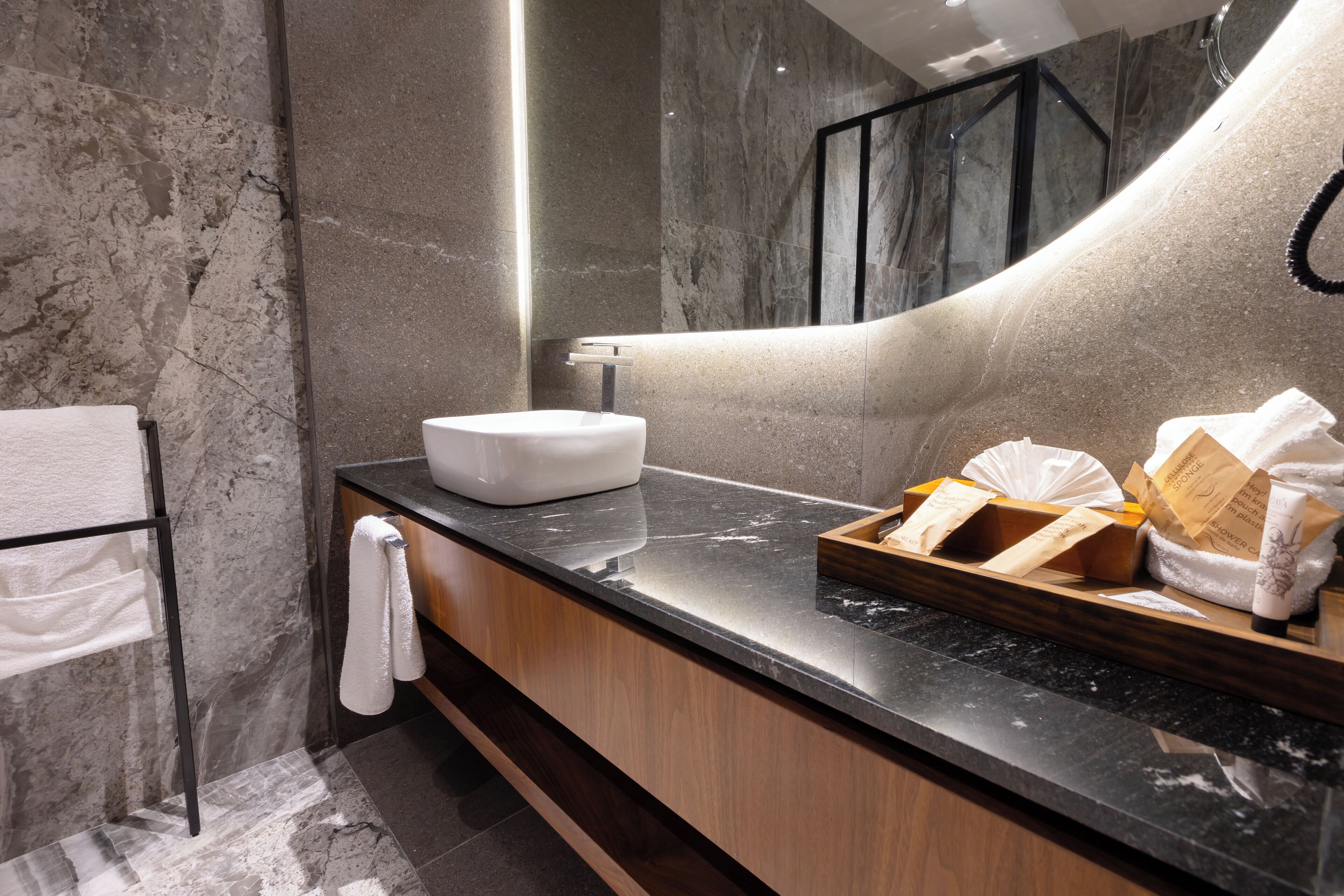 Un baño moderno con lavamanos de mármol, tocador de madera y un espejo grande.