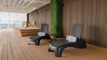 Un espacio de estar al aire libre techado con dos sillones, una mesita y un escenario.