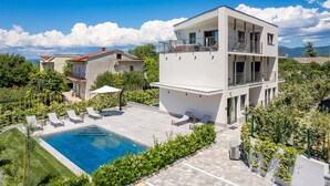 A modern multi-story building with a rooftop pool, surrounded by lush greenery and other residential buildings. - Awesome apartment in Omisalj (Omisalj)