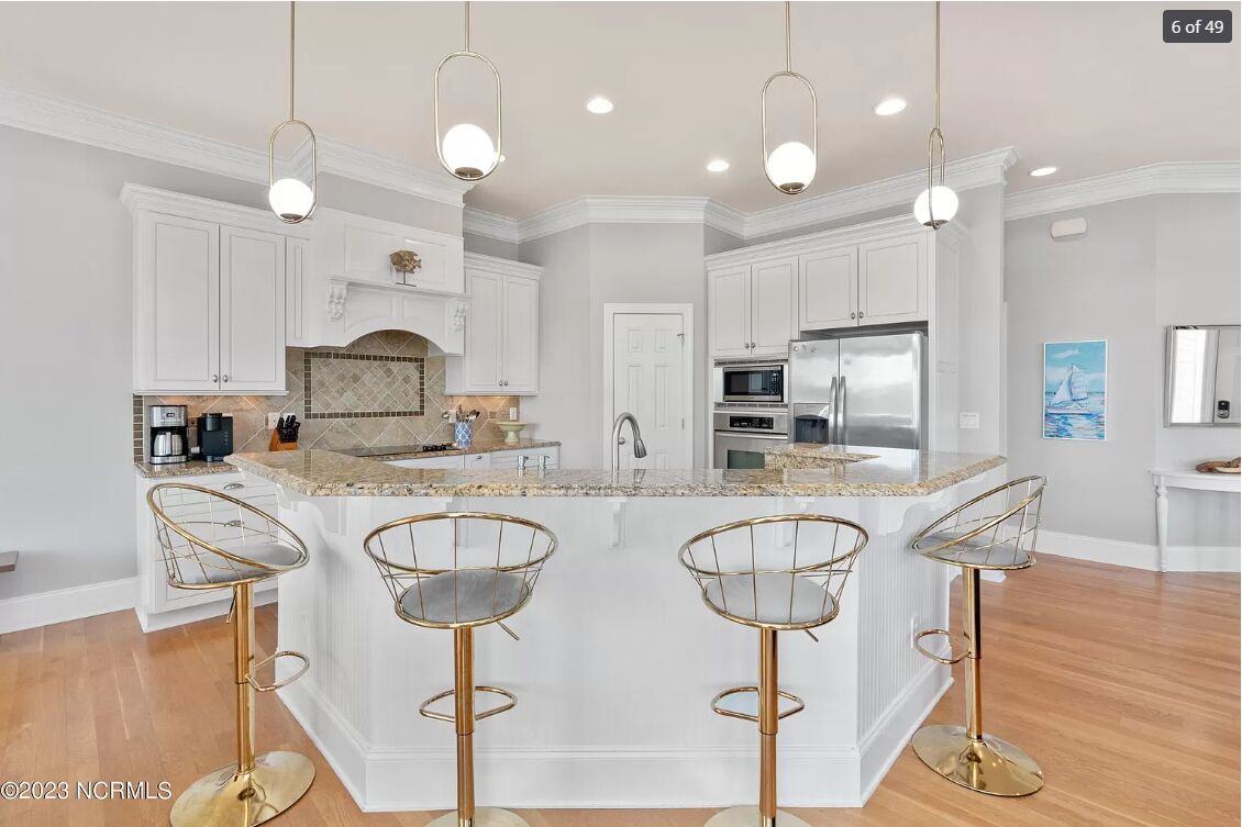 A spacious kitchen with white cabinetry, a large island with bar stools, stainless steel appliances, and pendant lighting.