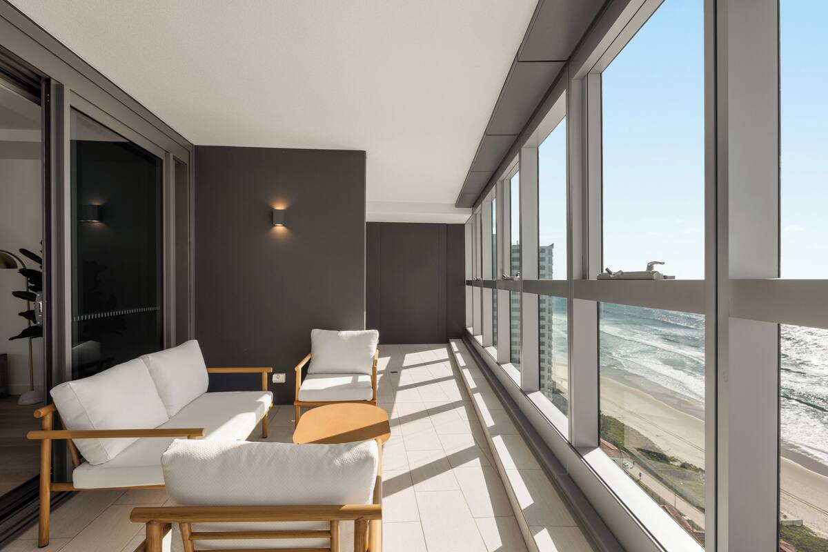 Ein moderner Balkon mit einer weißen Couch, zwei Stühlen und einem kleinen Tisch.