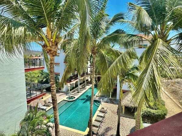 A pool area with palm trees, lounge chairs, and a building with balconies.