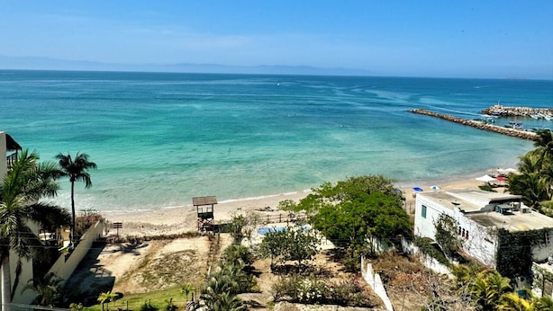 Une vue sur la côte, avec une plage, une eau d’un bleu limpide et une digue rocheuse.