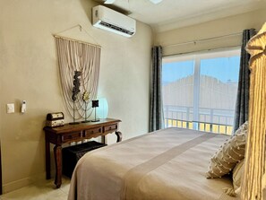 Habitación de hotel con una cama grande, un escritorio con lámpara, aire acondicionado y vistas a un edificio a través de la ventana.
