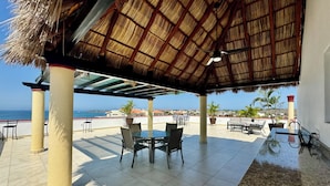 Une terrasse extérieure dotée d’un toit de chaume, une table ronde avec des chaises et une vue sur la mer.