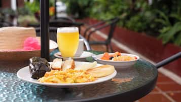 Ein Tisch mit Frühstücksartikeln, darunter Eier, Toast und einem Getränk, draußen mit Pflanzen im Hintergrund.