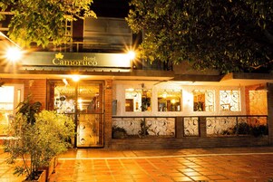 Entrada de un hotel con un cartel que dice "Hotel Camoruso", puerta de cristal y pavimento de baldosas.
