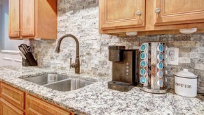 A kitchen with granite countertops, a stainless steel sink, wooden cabinets, a coffee maker, and a coffee storage container. - Pool vibes!  (Douglasville)
