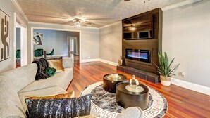 A spacious living room with a fireplace, a ceiling fan, and a flat-screen TV mounted on the wall. - Pool vibes!  (Douglasville)